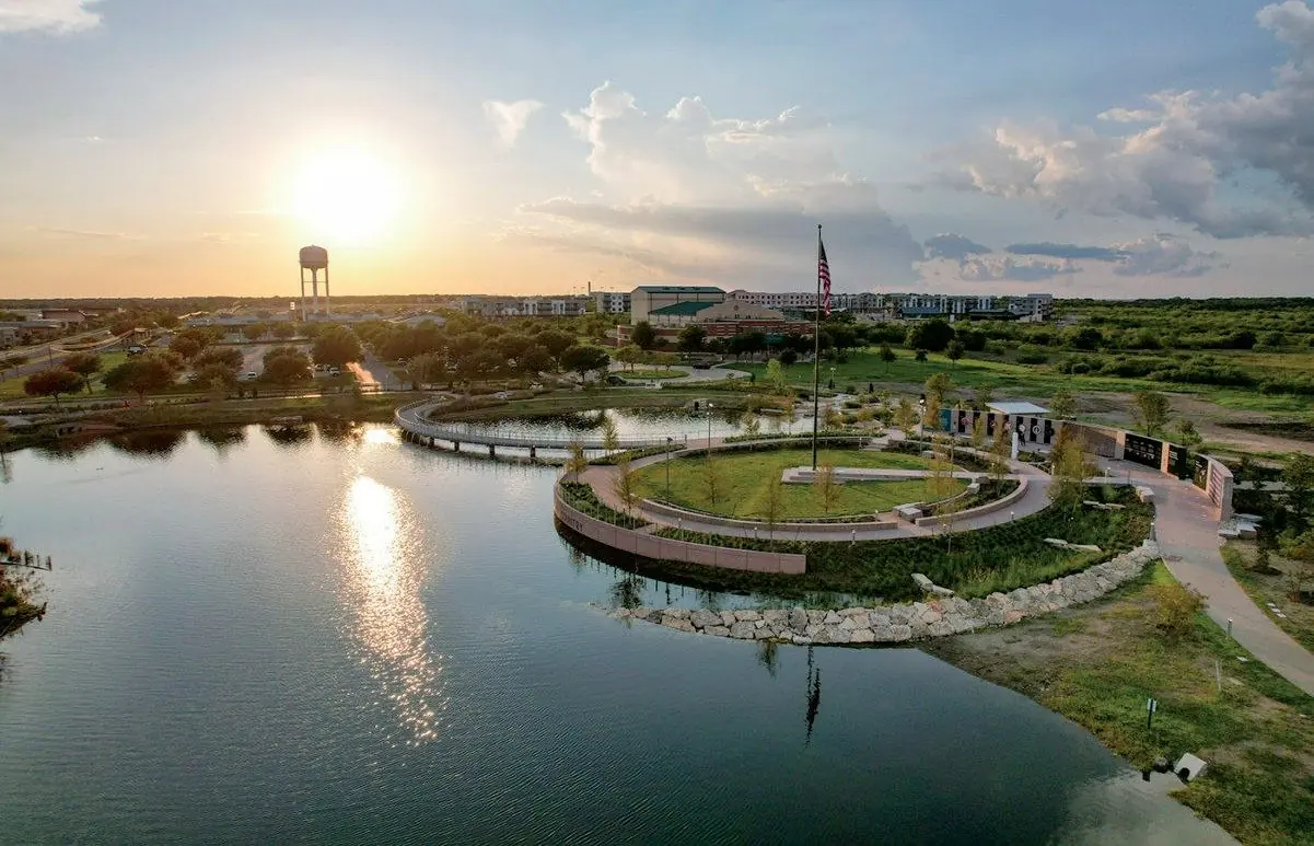 Aerial view of Kyle Heroes Memorial Park at sunset, with the lake, circular plaza and flag
